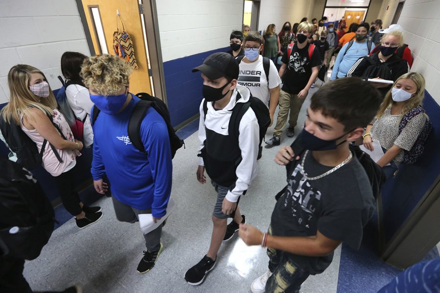 FILE - In this Aug. 6, 2020, file photo, Guntown Middle School eighth graders walk the halls to their next class as others wait in their assigned spots against the wall before moving into their next class during the first day back to school for the Lee County District in Guntown, Miss. As schools reopen around the country, their ability to quickly identify and contain coronavirus outbreaks before they get out of hand is about to be put to the test. (Adam Robison/The Northeast Mississippi Daily Journal via AP, File)